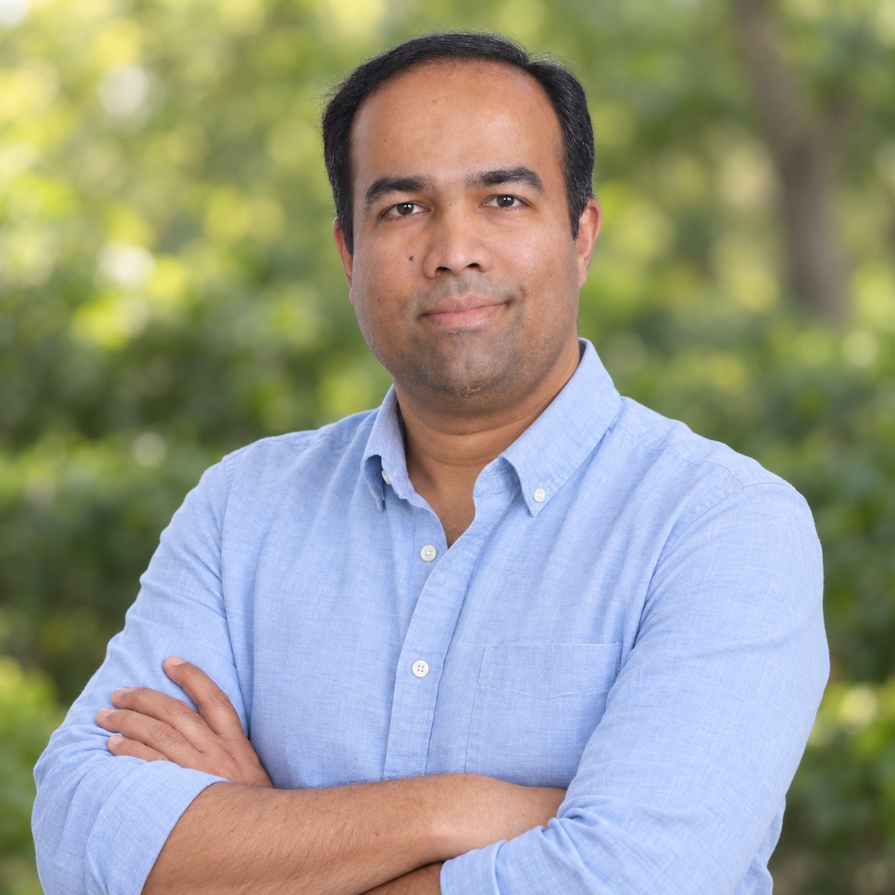 Joshua Cleetus in a light blue shirt, arms crossed outdoors